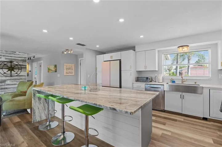Kitchen featuring stainless steel dishwasher, light wood-style flooring, a sink, and freestanding refrigerator  - Virtually Edited Image