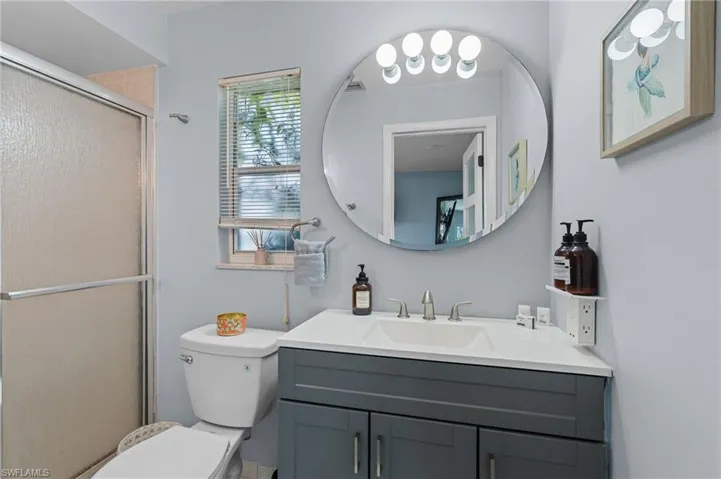 Bathroom featuring toilet, vanity, visible vents, and a shower with shower door  - Virtually Edited Image