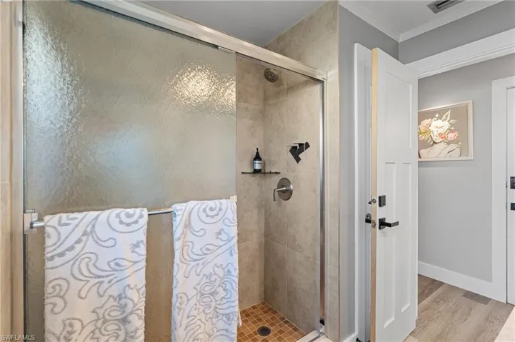 Full bath featuring baseboards, wood finished floors, ornamental molding, and a stall shower  - Virtually Edited Image