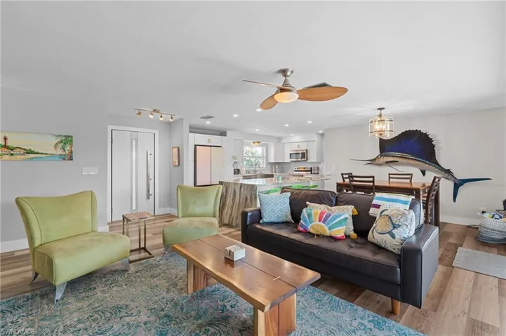 Living area with light wood-style floors, baseboards, and ceiling fan with notable chandelier  - Virtually Edited Image