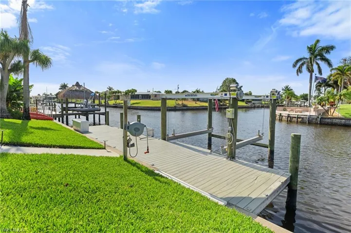 View of dock with a lawn, boat lift, and a water view  - Virtually Edited Image