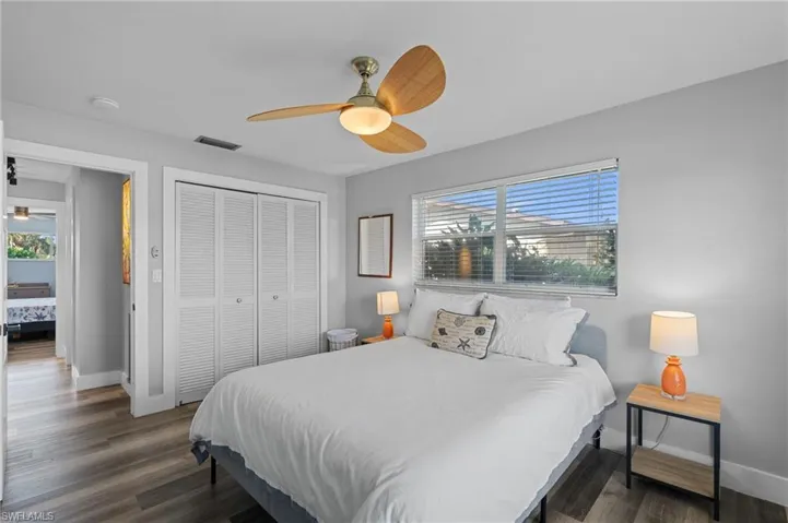 Bedroom with a closet, wood finished floors, visible vents, and multiple windows  - Virtually Edited Image