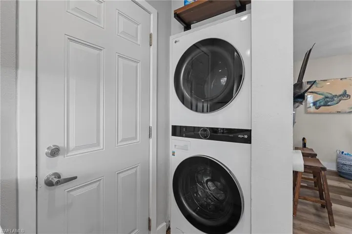 Clothes washing area featuring stacked washer / drying machine, wood finished floors, and laundry area  - Virtually Edited Image