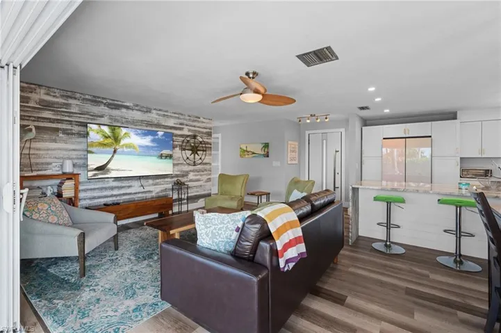 Living room featuring an accent wall, wooden walls, ceiling fan, dark wood finished floors, and recessed lighting  - Virtually Edited Image