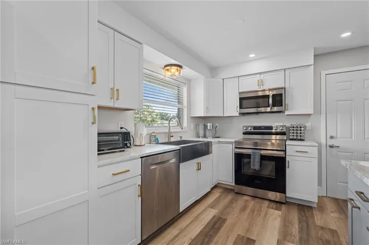 Kitchen featuring light wood finished floors, stainless steel appliances, a sink, recessed lighting, and white cabinetry  - Virtually Edited Image