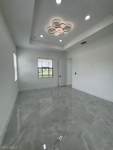 Empty room featuring a raised ceiling, recessed lighting, and marble finish floors