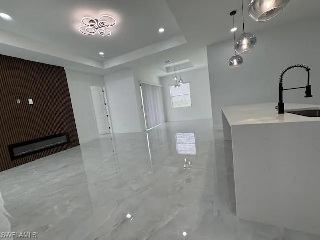 Unfurnished living room featuring light marble finish floors, a raised ceiling, recessed lighting, and a glass covered fireplace