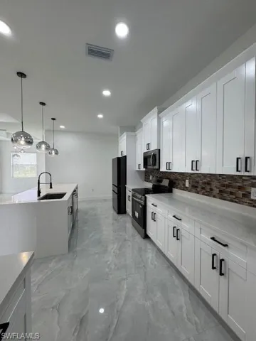 Kitchen featuring stove, backsplash, white cabinets, recessed lighting, and light marble finish flooring
