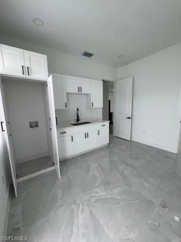 Kitchen featuring white cabinets, view of the Stackable washing machine closet, light countertops, and light marble finish flooring