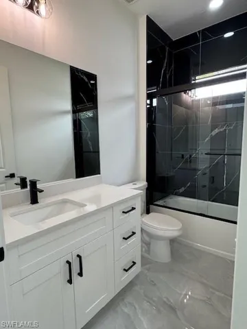 Bathroom with shower / bath combination with glass door, vanity, marble finish flooring, and recessed lighting