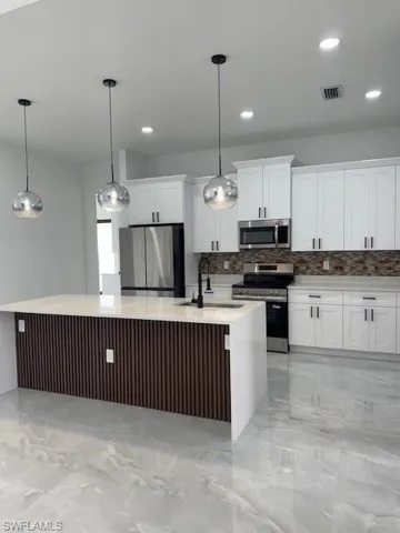 Kitchen with light marble finish flooring, stove, decorative backsplash, fridge, and an island with sink