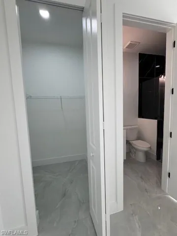 Bathroom featuring marble look tile flooring, a spacious closet, and recessed lighting