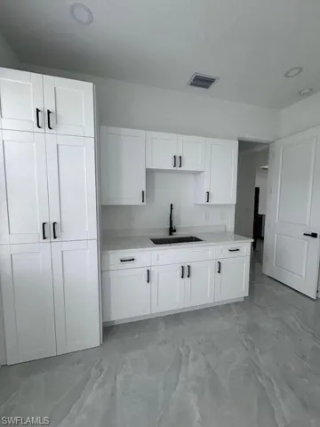 Kitchen featuring light marble finish flooring, white cabinets, Stackable washing machine closet, light countertops