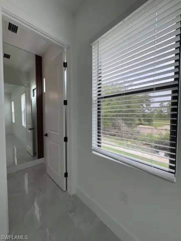 Primary Bathroom's entrance with large costume mirror, marble finish floors and plenty of natural light