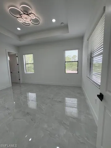 Empty room featuring a tray ceiling, light marble finish flooring, and recessed lighting