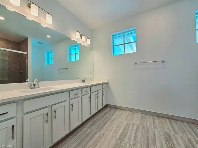 Bathroom with a stall shower, double vanity, healthy amount of natural light, baseboards, and recessed lighting