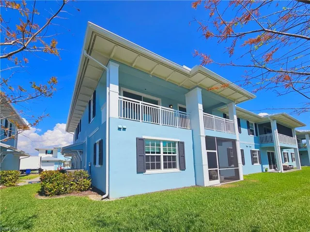 Rear view of property featuring stucco siding, a lawn, and a balcony