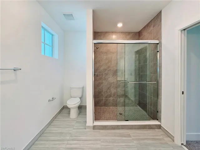 Full bath featuring a stall shower, toilet, and baseboards