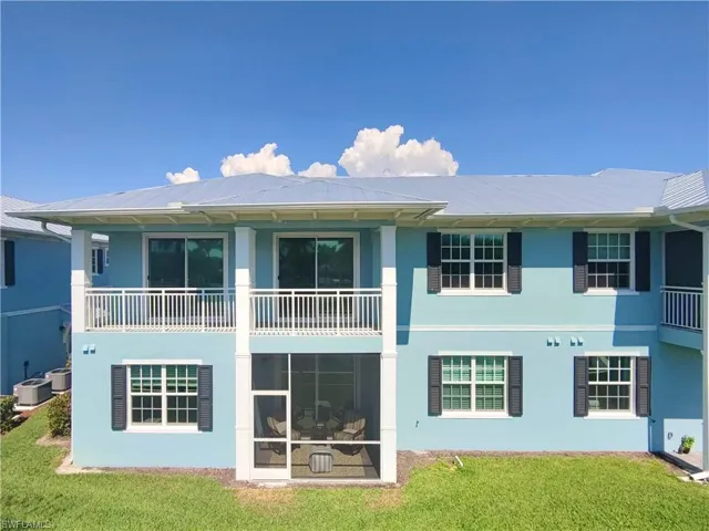 Rear view of house featuring stucco siding, a balcony, and a lawn