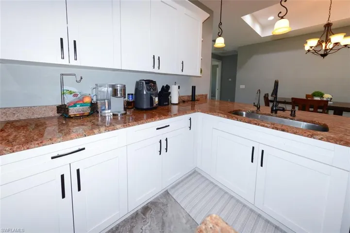 Kitchen with white cabinets, dark stone counters, a chandelier, and hanging light fixtures