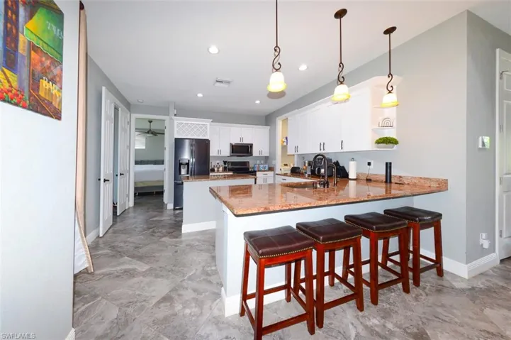 Kitchen with white cabinetry, a breakfast bar area, decorative light fixtures, a peninsula, and appliances with stainless steel finishes