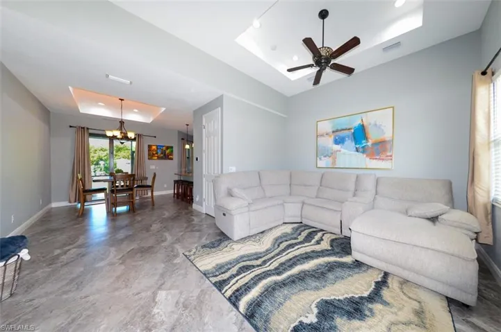 Living area featuring a raised ceiling, a chandelier, and ceiling fan