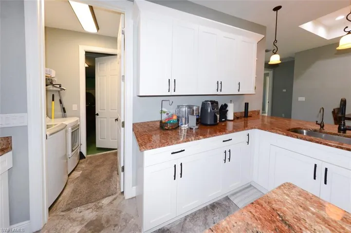 Kitchen with white cabinetry, washing machine and clothes dryer, light stone countertops, and decorative light fixtures