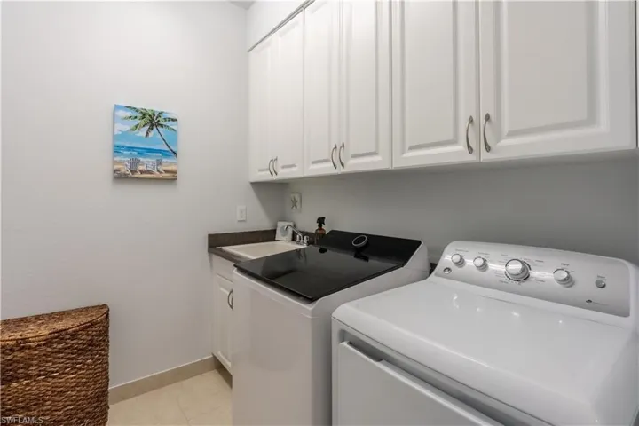 Upstairs laundry area featuring white shaker-style cabinetry, a built-in utility sink with a dark countertop, and light-toned floor tile