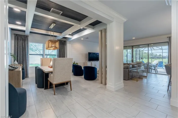 Open-concept living space featuring light wood-finish flooring, a coffered ceiling with recessed lighting, and a dining area with a contemporary chandelier