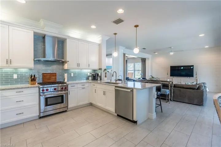 Contemporary kitchen featuring white cabinetry, a stainless steel range with matching hood, a blue glass tile backsplash, and light-toned tile flooring