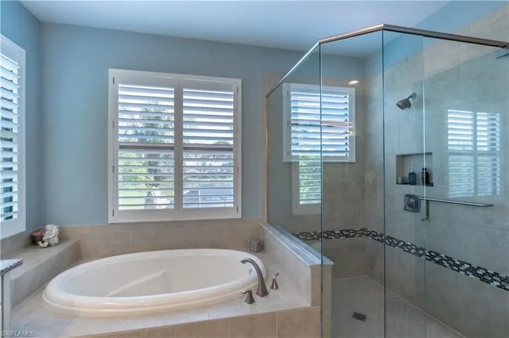 Soaking tub with a tiled surround, framed by multiple windows with white plantation shutters