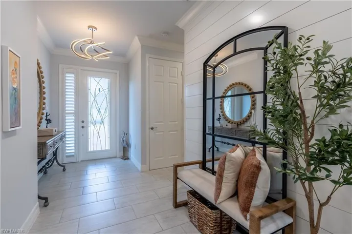 Entryway featuring large format tile flooring, decorative glass front door, contemporary ceiling light fixture, and shiplap accent wall