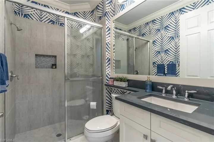 Bathroom featuring a glass-enclosed shower with tile surround and mosaic accent niche, a vanity with an integrated sink and dark countertop, and decorative wall covering