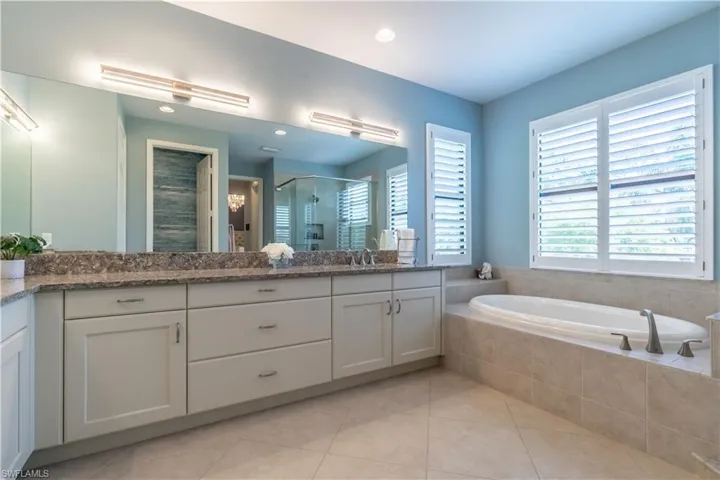 Bathroom featuring a dual vanity with a large mirror, light cabinetry, and stone countertops