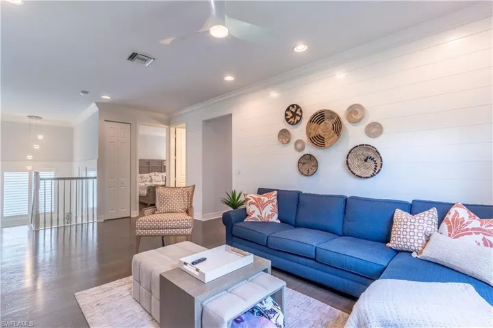 Spacious upper-level living area featuring hardwood flooring, shiplap accent wall, recessed lighting, ceiling fan, and a painted railing overlooking the lower level