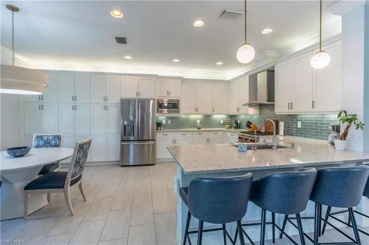 Spacious kitchen featuring an expansive island with stone countertop, stainless steel appliances, full-height white cabinetry, and a subway tile backsplash