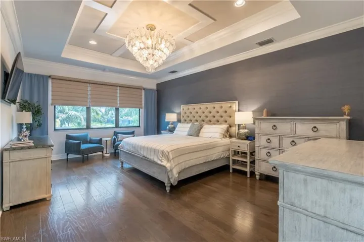Spacious room featuring rich wood-finish flooring, a tray ceiling with crown molding, and a chandelier