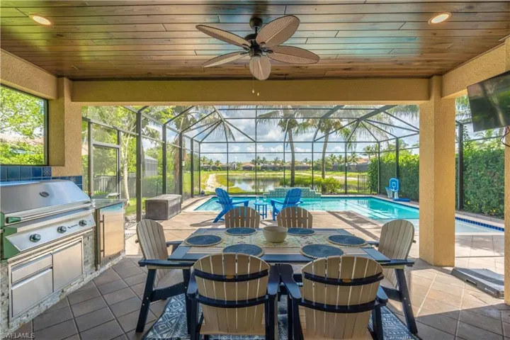 Covered patio featuring an outdoor kitchen with stainless steel grill, a screened-in swimming pool, and a tranquil water feature beyond