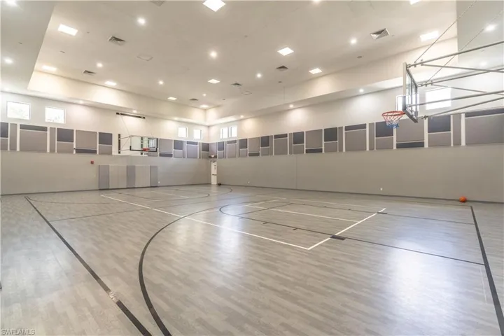 Indoor sports court featuring a wood-finish floor with court markings, recessed lighting, high ceilings, perimeter windows, and wall-mounted sound dampening panels
