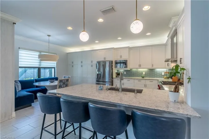 Kitchen featuring a large central island with seating, white shaker cabinetry, stainless steel appliances, a light blue subway tile backsplash, and recessed lighting
