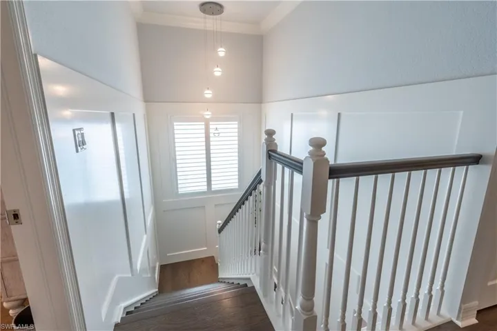 Staircase featuring wood-finish flooring, white board and batten paneling, and a dark wood handrail