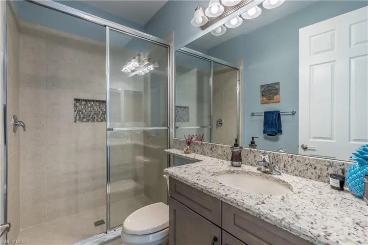 Bathroom featuring a glass-enclosed shower with tile surround and mosaic accent, a vanity with a light-toned countertop and integrated sink, a built-in mirror, and a white panel door