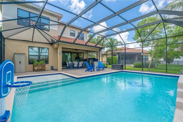 Screened swimming pool with a stone paver deck, covered patio, integrated steps, and a perimeter safety fence