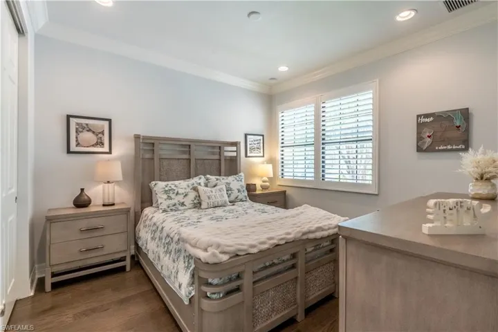Bedroom featuring wood-finish flooring, crown molding, recessed lighting, a window with plantation shutters, and a paneled door