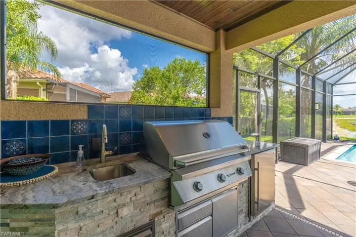 Outdoor kitchen featuring a built-in stainless steel grill, integrated sink, and stone-finish countertop