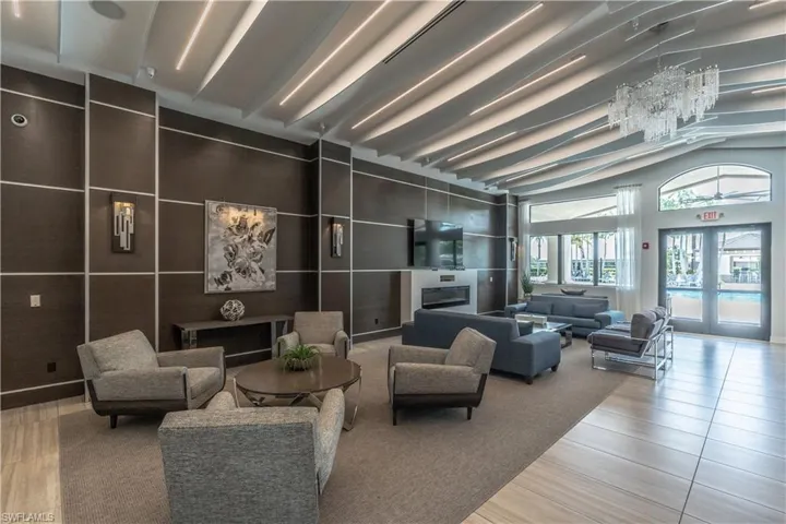 Spacious common area featuring a distinctive ceiling design with integrated lighting, wood-paneled accent walls, a built-in fireplace, and expansive windows