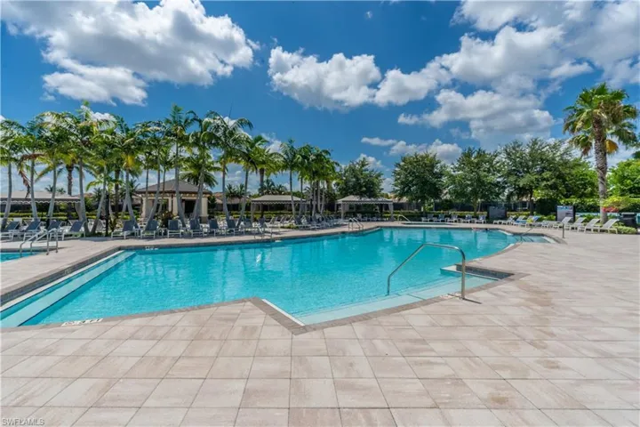 Resort-style swimming pool featuring a spacious paver deck, multiple entry steps with handrails, and surrounding palm trees