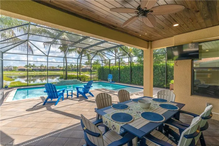 Screened outdoor living area featuring a wood-finish ceiling with a ceiling fan, a built-in television, a paver patio, a swimming pool with a water feature, and a tranquil water view