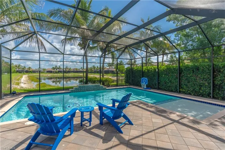 Screened-in swimming pool with a sun shelf and water feature, complemented by a paver deck and lush green privacy hedging