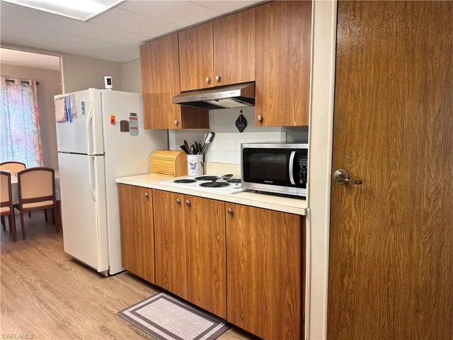 Kitchen with wall chimney exhaust hood, light wood-type flooring, decorative backsplash, and white appliances